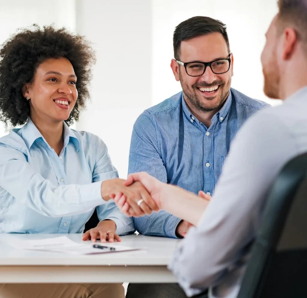 Professionnels diversifiés se serrant la main autour d'un bureau dans un bureau lumineux, illustrant un partenariat et une collaboration réussie.
